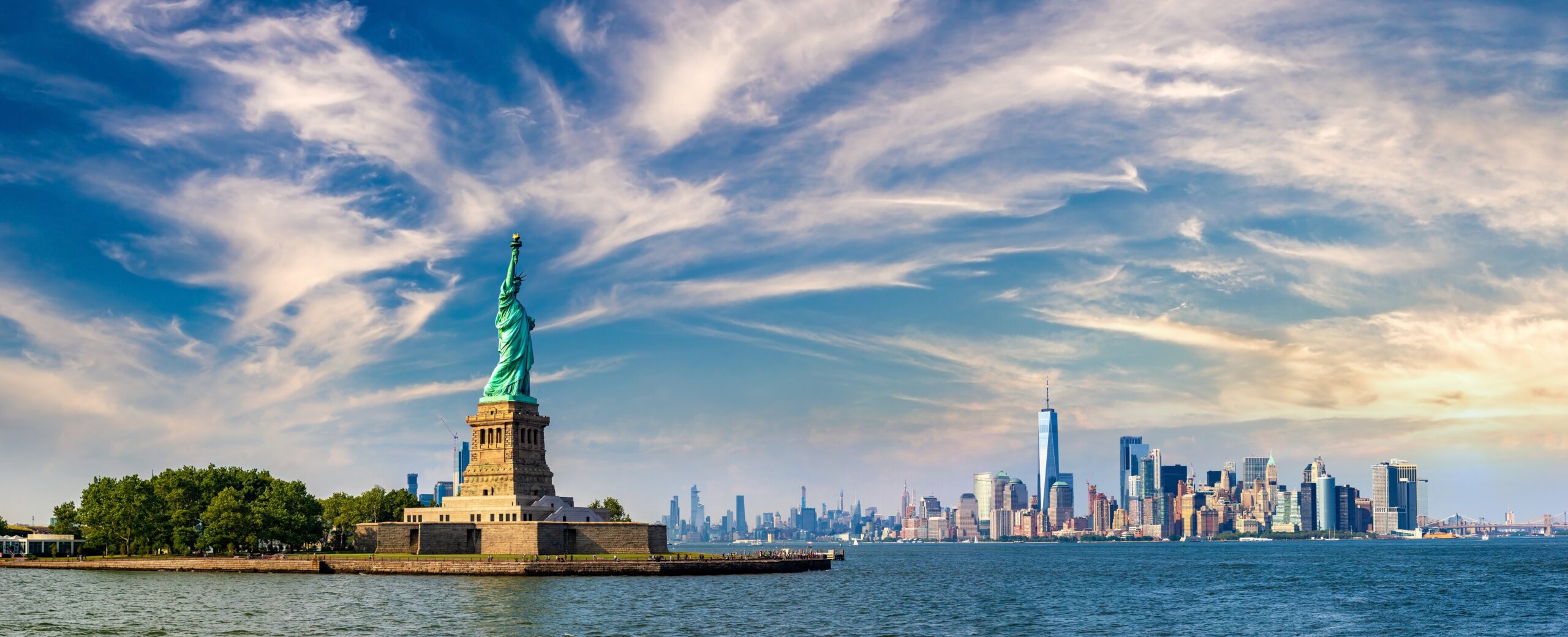 Statue of Liberty with New York City skyline under a bright sky.